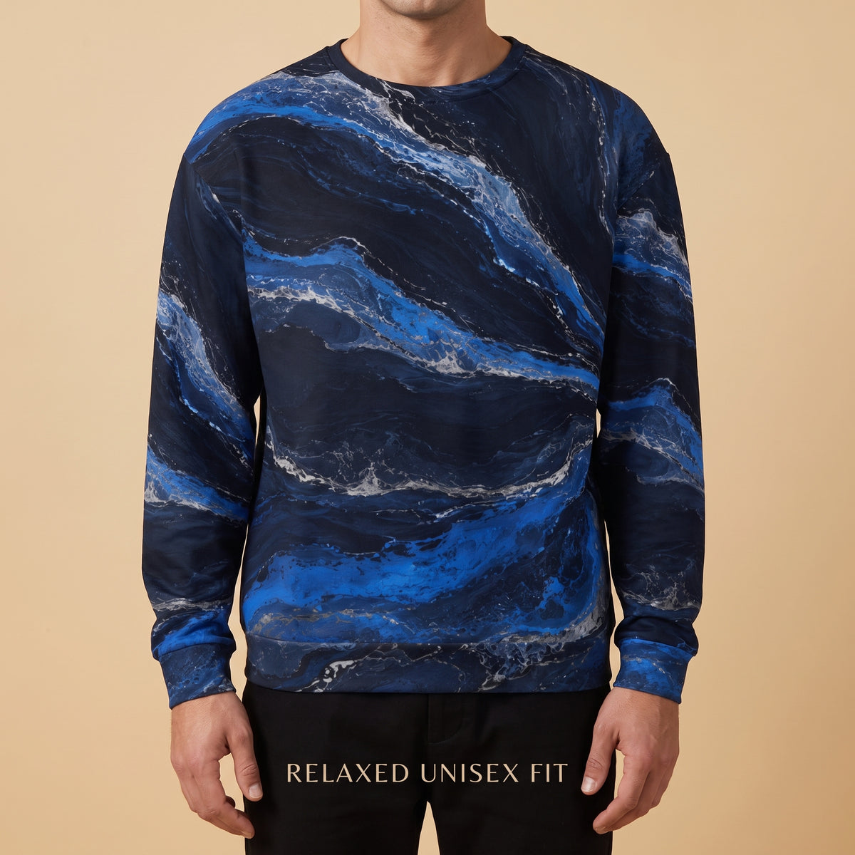 A man wearing a long-sleeve crewneck sweatshirt with a blue and navy marble pattern, paired with black pants, against a solid beige background.