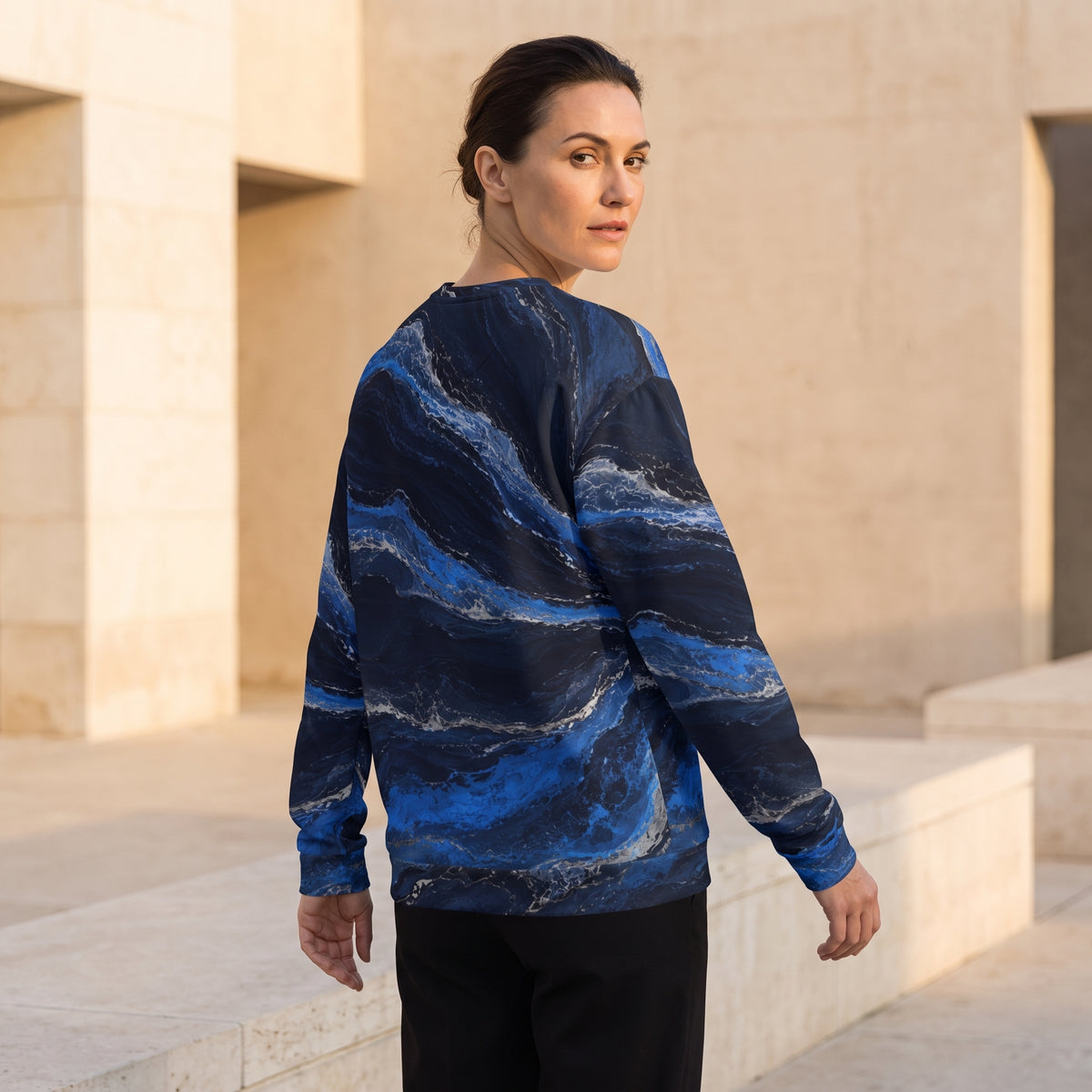 A woman wearing a long-sleeve crewneck sweatshirt with a blue and navy marble pattern, standing outdoors in front of beige stone architectural columns.
