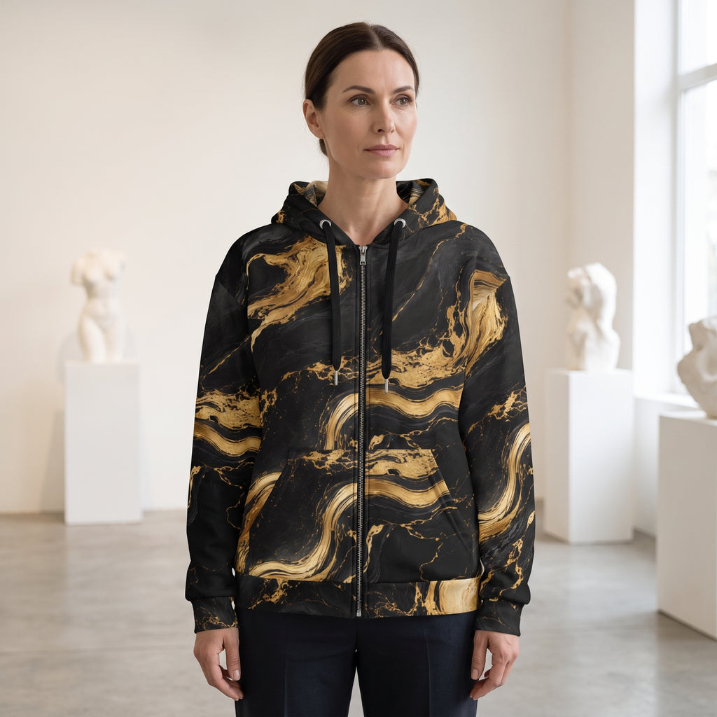 A woman wearing a black zip-up hoodie with a gold marble swirl pattern, standing in a bright, modern art gallery with white sculpture busts in the background.