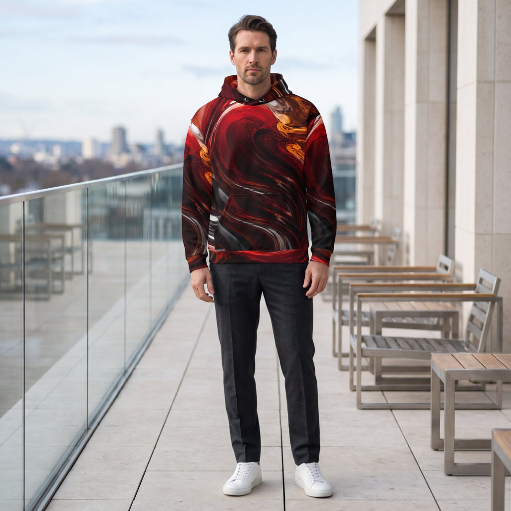 A man stands on a modern outdoor balcony wearing a pullover hoodie with a bold red, black, and orange abstract swirl pattern, paired with dark gray jeans and white sneakers.