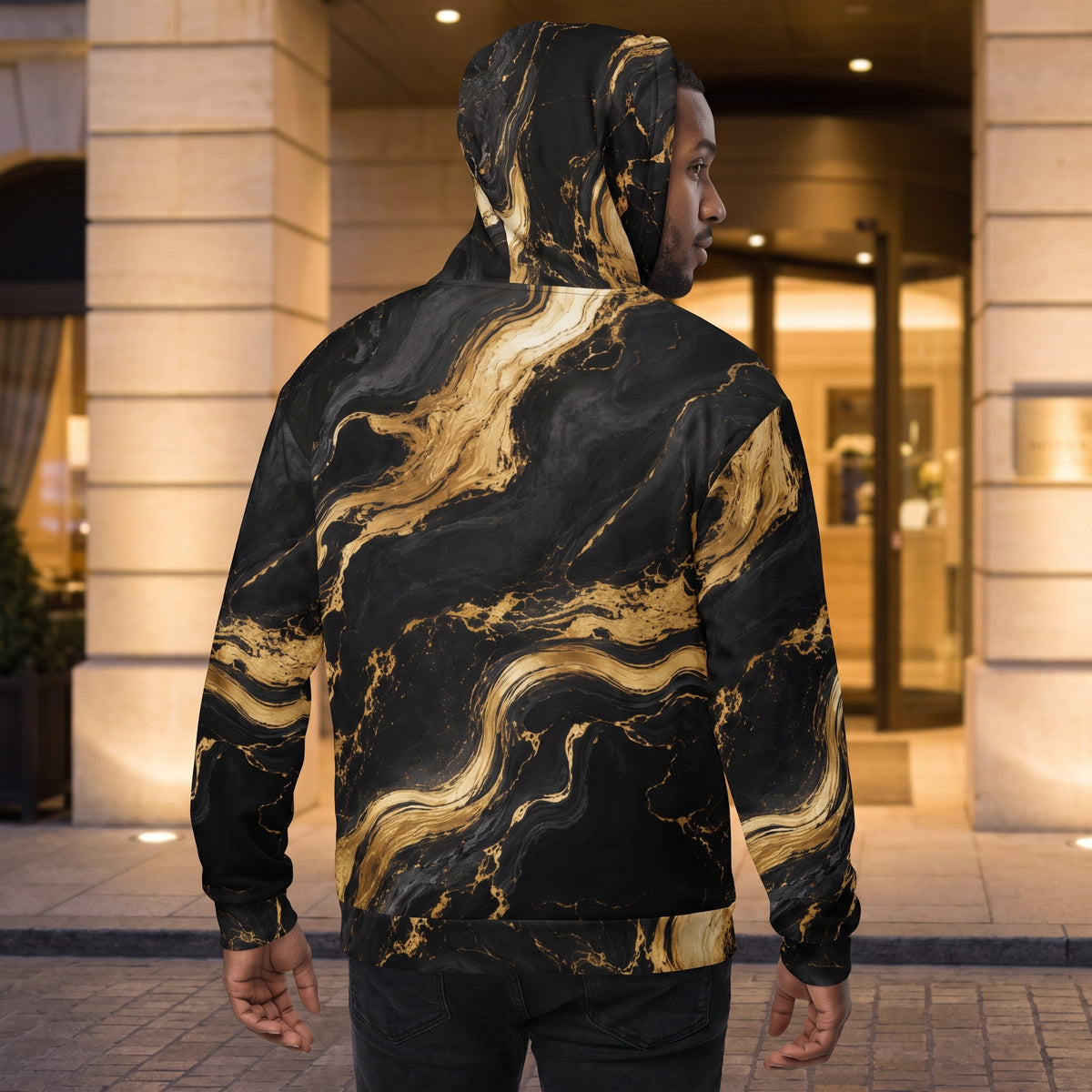 A man wearing a black and gold marble-patterned hoodie, shown from the back in an outdoor setting in front of a building entrance.
