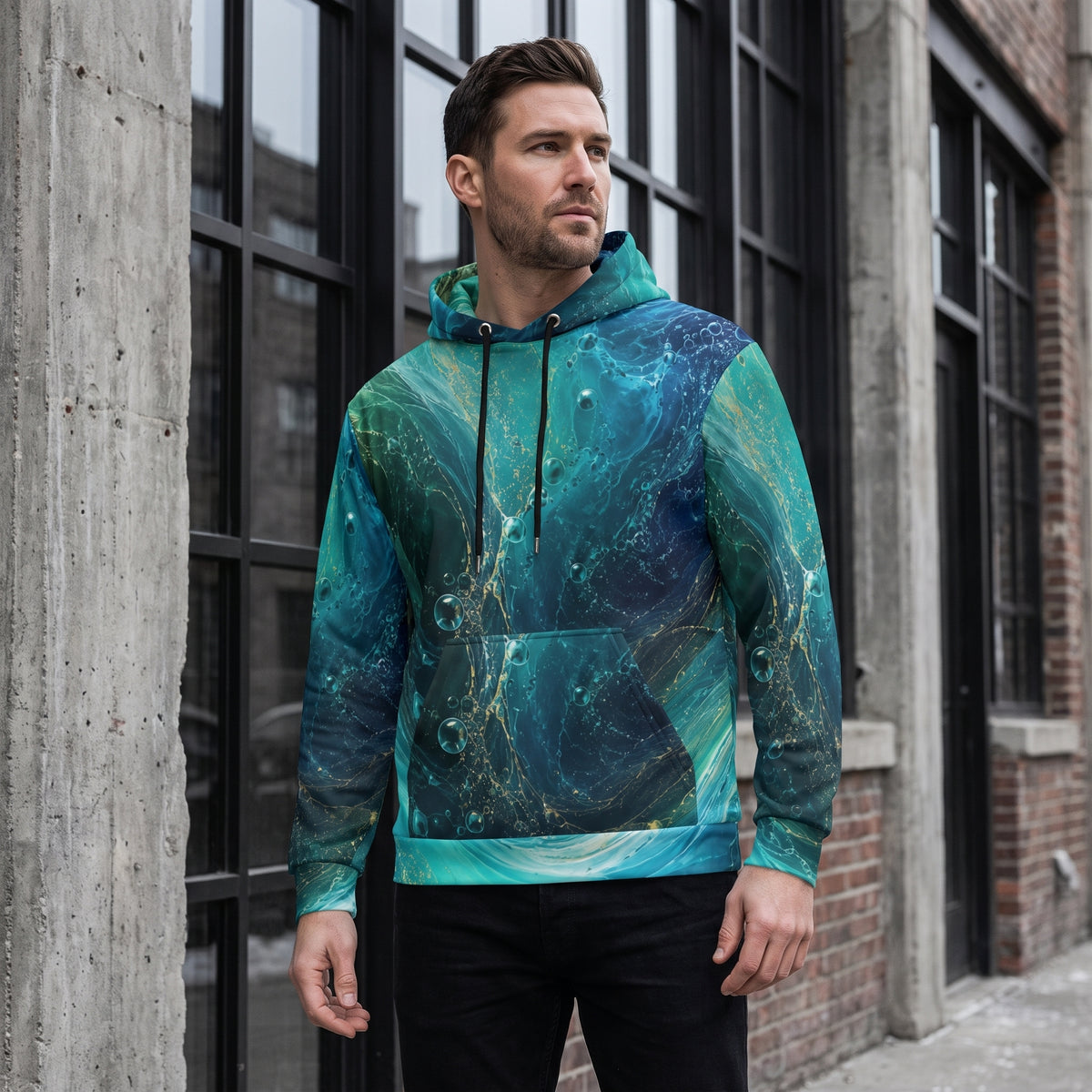 A man wearing a teal and blue marbled hoodie with gold glitter accents, standing in front of an industrial brick building with large black-framed windows.