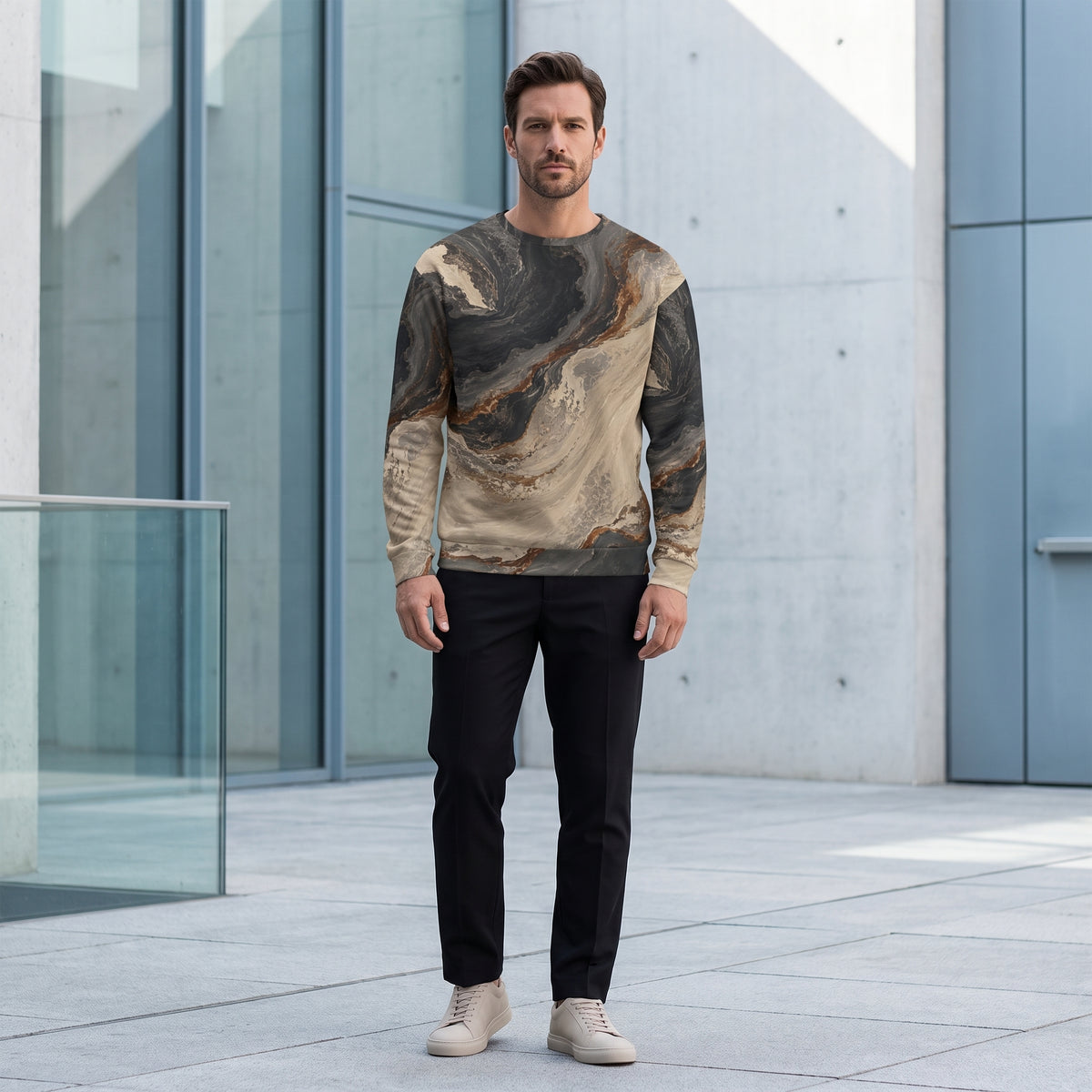 A man wearing a long-sleeve crewneck sweatshirt with a marbled abstract pattern in beige, brown, and black, paired with black pants and beige sneakers, standing in front of a modern concrete building.
