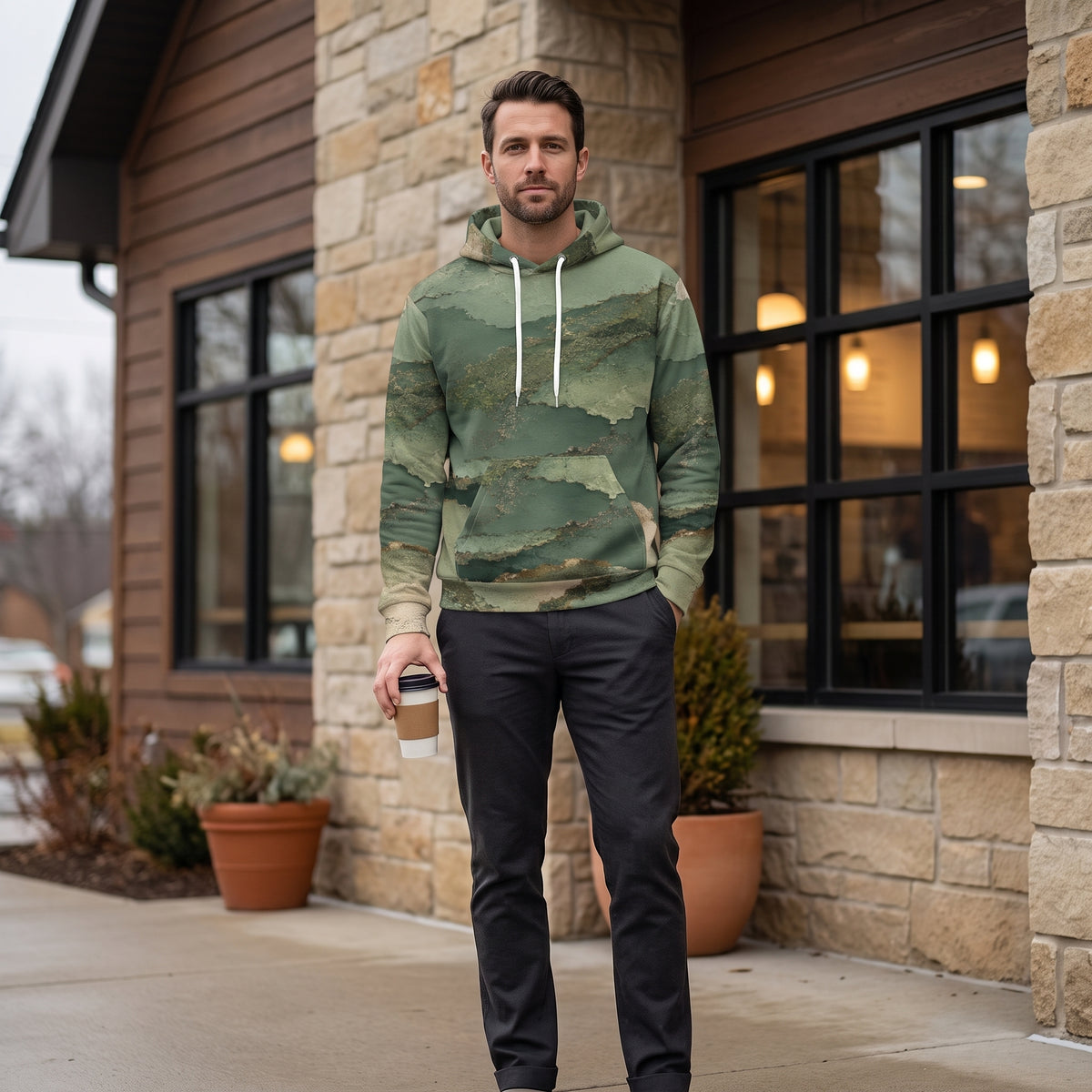 Man wearing the Verdant Terrain hoodie in a café – sage, olive and gold abstract print