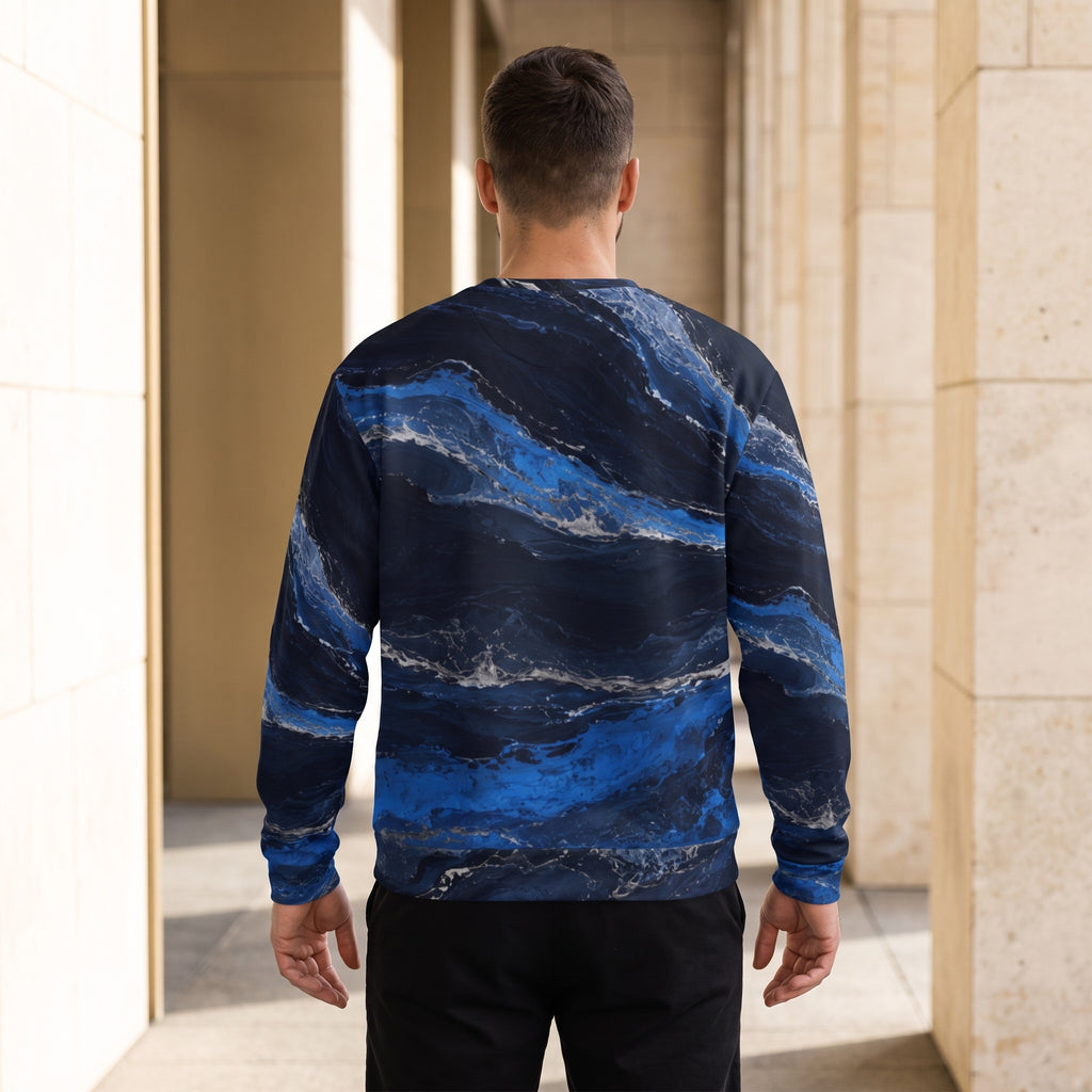A man viewed from behind wearing a long-sleeve crewneck sweatshirt with a blue and navy marble pattern, standing in a modern architectural corridor with beige stone columns.