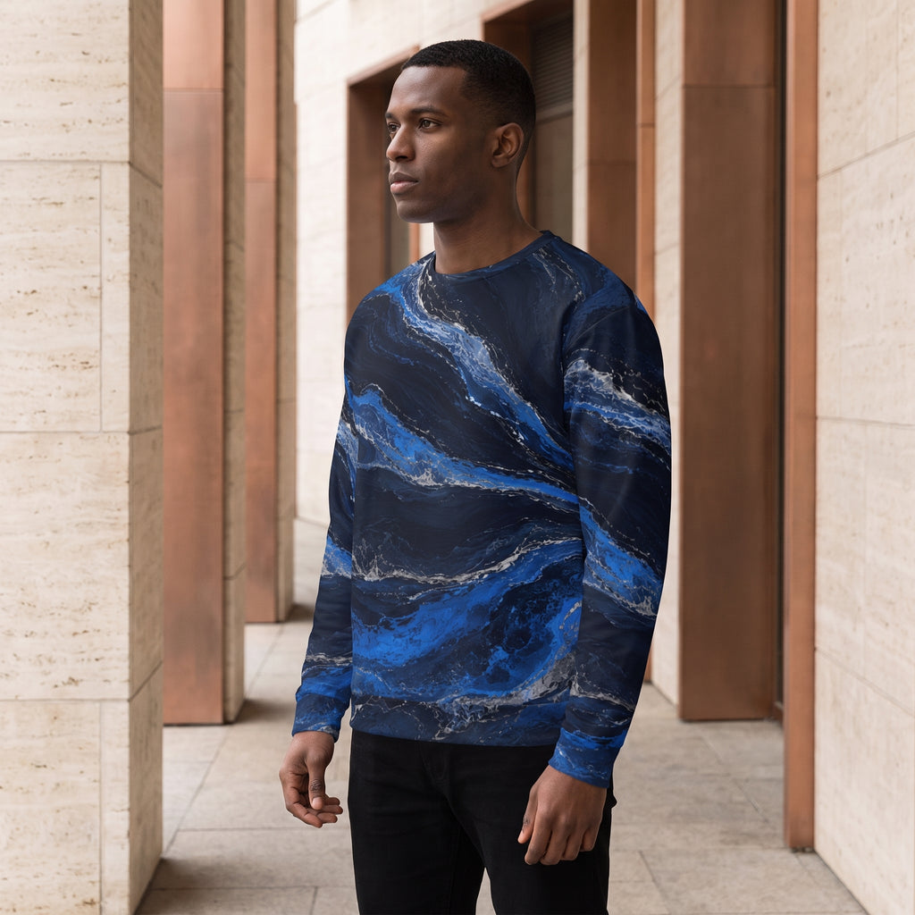 A man wearing a long-sleeve crewneck sweatshirt with a blue and navy marble pattern, standing in a modern architectural walkway with beige stone columns.