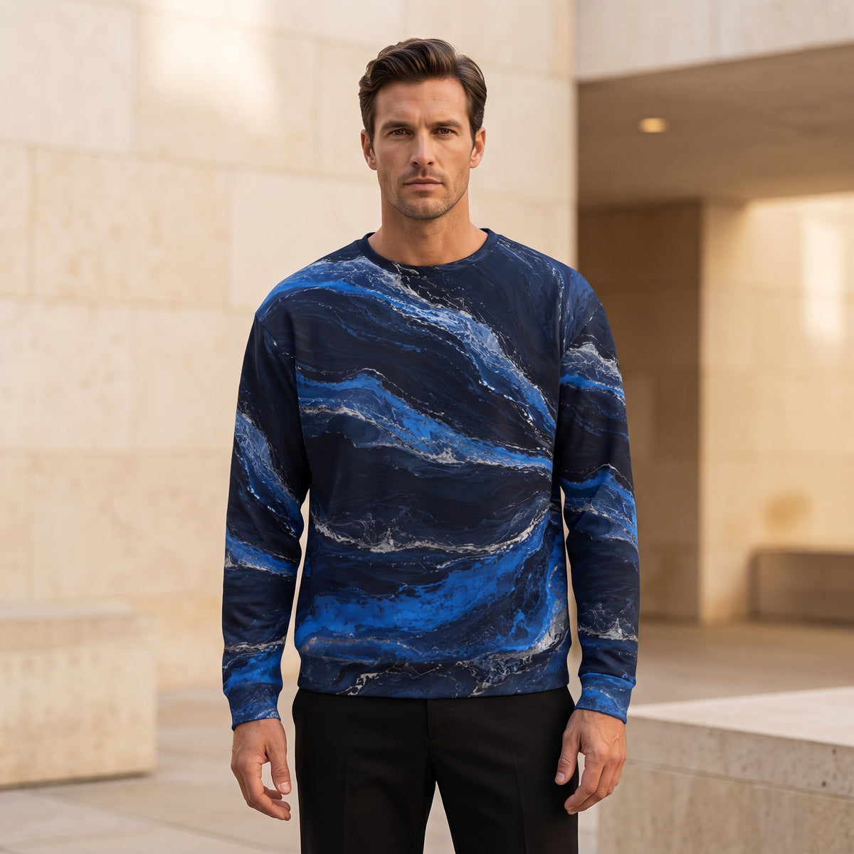 A man wearing a long-sleeve crewneck sweatshirt with a blue and navy marble pattern, standing in front of a beige stone building.
