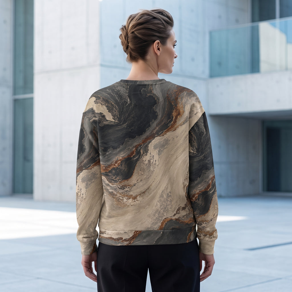 A woman viewed from behind wearing a long-sleeve crewneck sweatshirt with a marbled abstract print in beige, brown, and charcoal gray, set against a modern concrete building background.