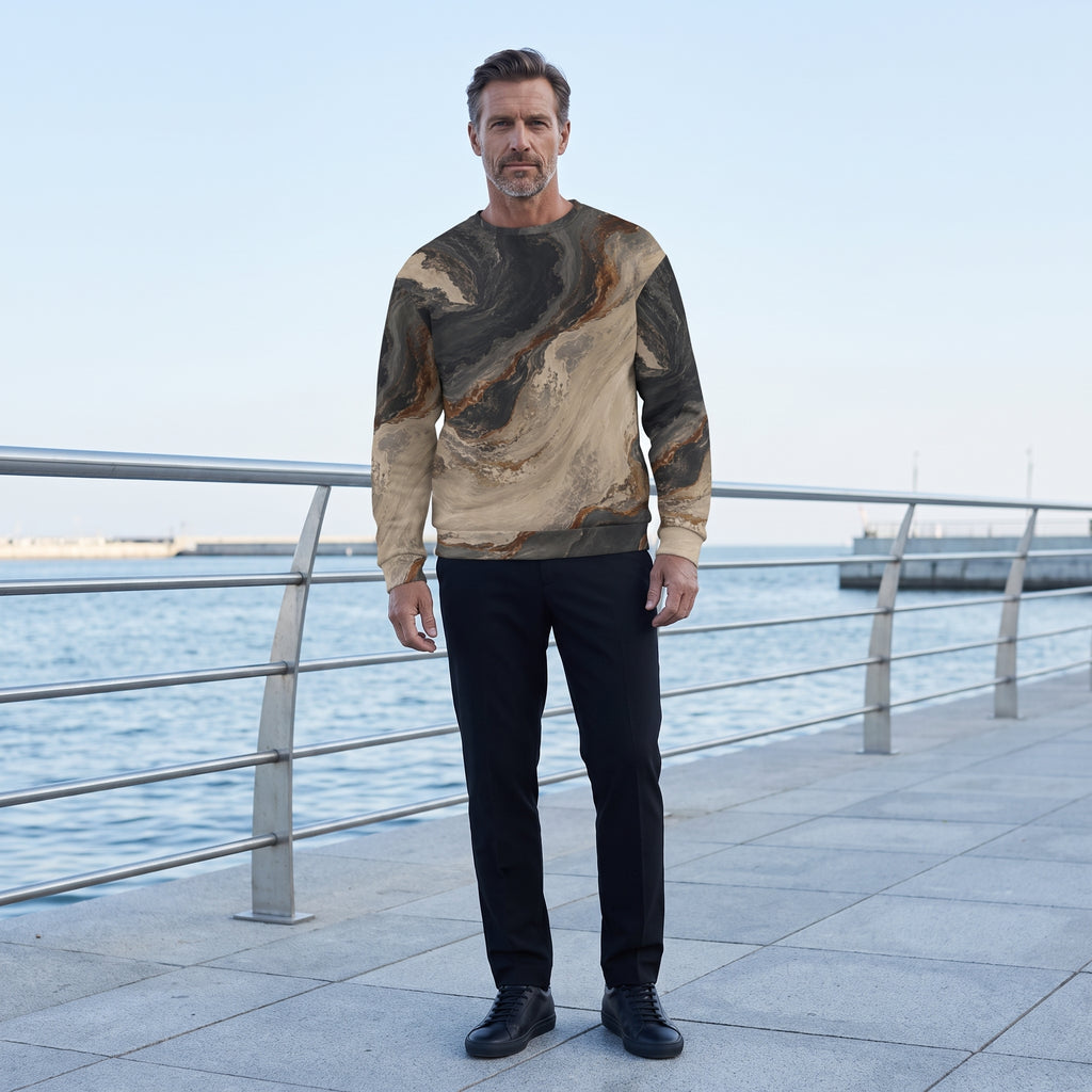 A man stands on a waterfront promenade wearing a long-sleeve crewneck sweatshirt with a brown and beige marbled pattern, paired with black trousers and black shoes.