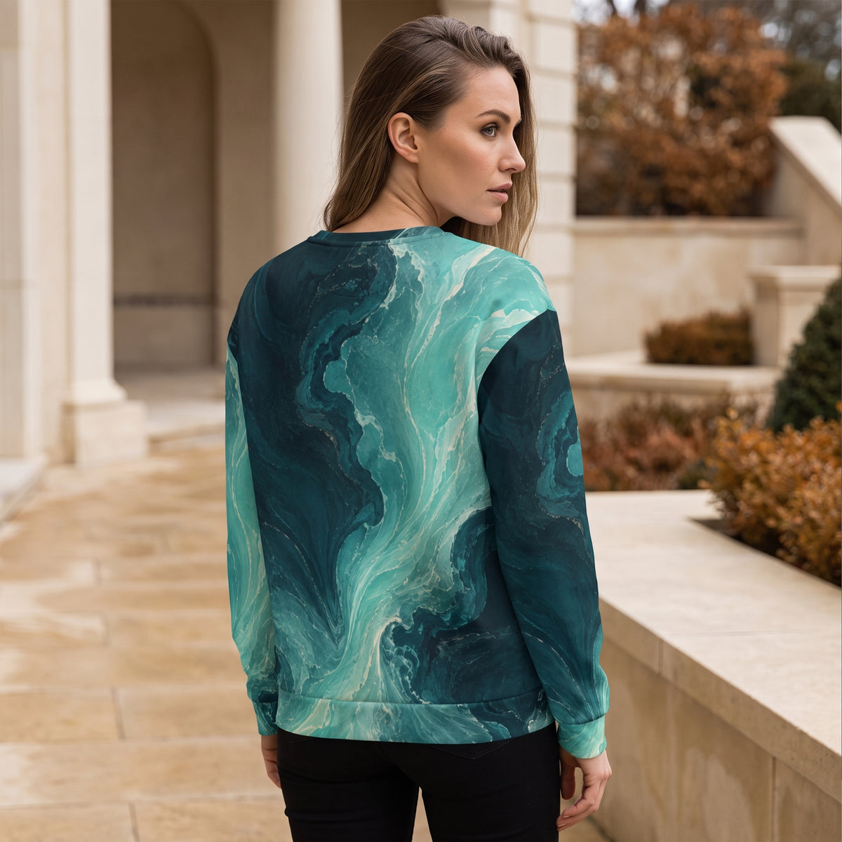 A woman wearing a long-sleeve crewneck sweatshirt with a teal and dark green marble swirl pattern, photographed from behind in an outdoor architectural setting.