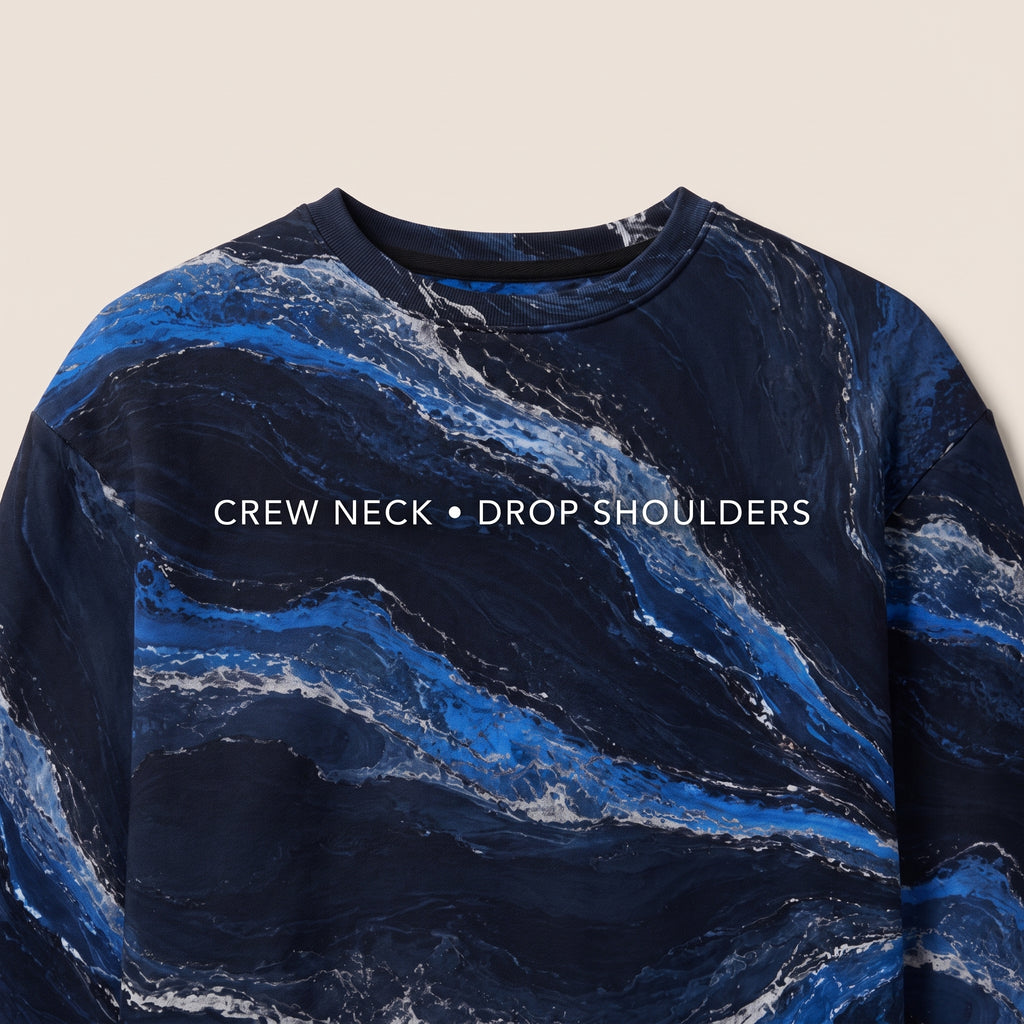 A close-up of a crew-neck sweatshirt with a blue and navy marble pattern and white text reading 'CREW NECK • DROP SHOULDERS' across the chest, shown against a light beige background.
