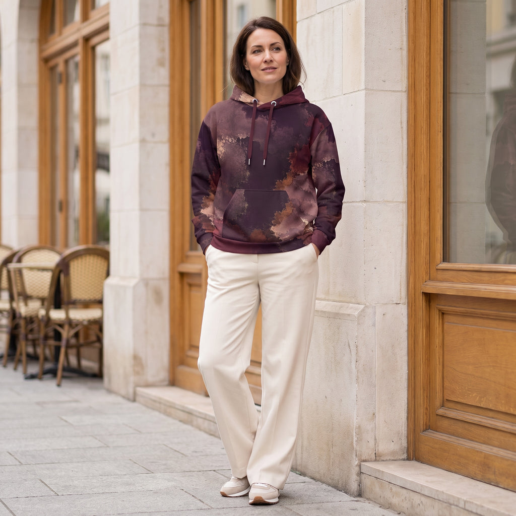 Woman wearing the Ember Eclipse hoodie in a café – burgundy, plum and copper abstract print